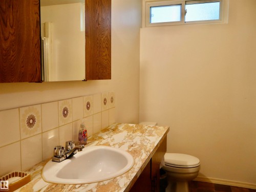 Bathroom featuring a wood-finish vanity with an integrated sink and a patterned countertop - 5530 46 Street, Barrhead, AB 