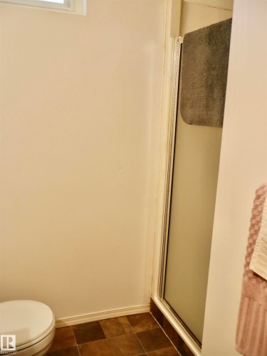 Bathroom featuring a white toilet, frosted glass shower enclosure, and earth-toned tile flooring - 5530 46 Street, Barrhead, AB 
