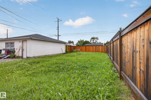 Spacious backyard with a wood privacy fence and a detached garage featuring white siding and a dark shingle roof - 9315 132A Avenue, Edmonton, AB 