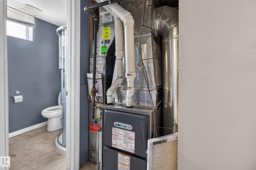 HVAC system with visible ductwork and associated piping, featuring a bathroom beyond with a toilet, a curved glass shower enclosure, and a frosted window - 9315 132A Avenue, Edmonton, AB 