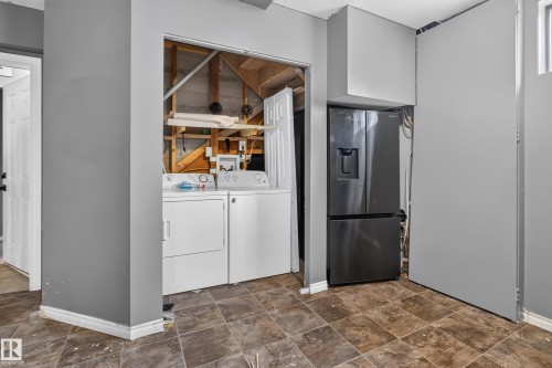 Utility area featuring durable tile flooring, a dark stainless steel refrigerator with an external dispenser, and a dedicated laundry alcove with washer and dryer hookups - 9315 132A Avenue, Edmonton, AB 