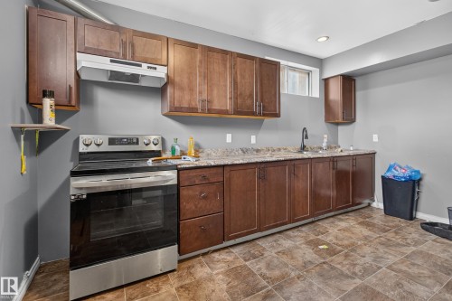 Kitchen area featuring extensive wood-finish cabinetry, a stainless steel range with overhead ventilation, a single basin sink with a gooseneck faucet, durable countertop surfaces, and patterned tile flooring - 9315 132A Avenue, Edmonton, AB 