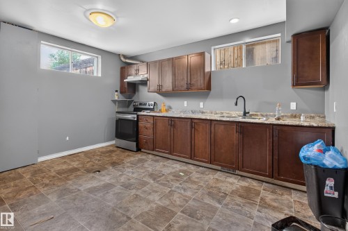 Kitchen area featuring extensive wood-finish cabinetry, stainless steel appliances, and a dark tile-look flooring - 9315 132A Avenue, Edmonton, AB 