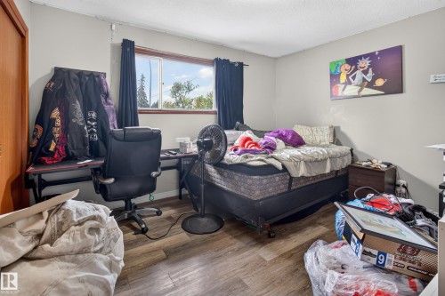 Bedroom featuring wood-finish flooring, a window with black curtains, light gray walls, and a built-in closet with a wood-panel door - 9315 132A Avenue, Edmonton, AB 