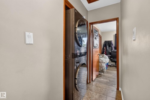 Dedicated laundry area featuring a stacked washer and dryer unit, neutral wall paint, and wood-finish door frames - 9315 132A Avenue, Edmonton, AB 
