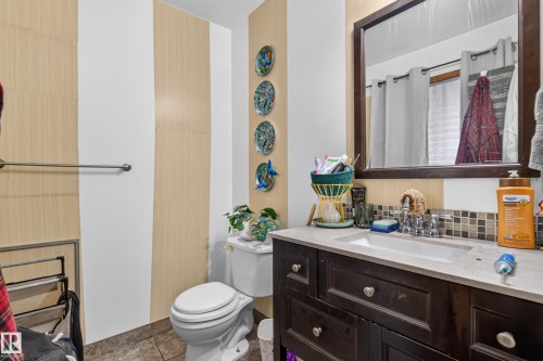 Bathroom featuring wood-finish accent wall paneling, a dark wood-finish vanity with a light-toned countertop and integrated sink, a rectangular framed mirror, and a mosaic tile backsplash - 9315 132A Avenue, Edmonton, AB 