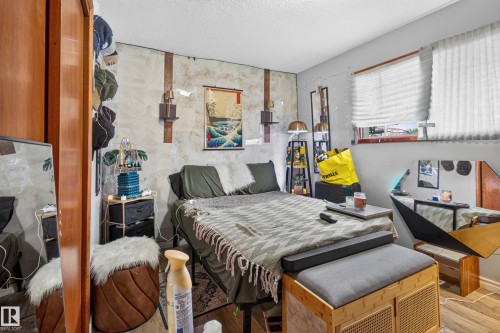 Bedroom featuring wood-finish flooring, a window with horizontal blinds, and a textured accent wall - 9315 132A Avenue, Edmonton, AB 