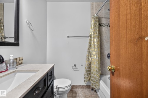 Bathroom featuring a dark wood vanity with a light-toned countertop, a rectangular sink, and a multi-toned tile backsplash - 9315 132A Avenue, Edmonton, AB 