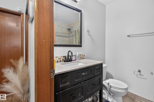 Bathroom featuring a dark wood-finish vanity with an integrated sink, a dark framed mirror, and a tiled shower enclosure - 9315 132A Avenue, Edmonton, AB 