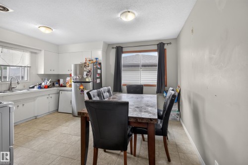 Kitchen and dining area featuring tiled flooring, a window with horizontal blinds, white cabinetry, a double basin sink, and ceiling-mounted light fixtures - 9315 132A Avenue, Edmonton, AB 