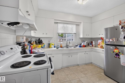 Kitchen featuring white cabinetry, tile backsplash, laminate countertops, and tile flooring - 9315 132A Avenue, Edmonton, AB 