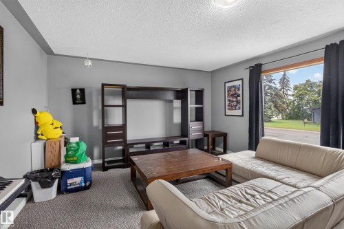 Carpeted living area featuring a large window, light gray walls, and a textured ceiling - 9315 132A Avenue, Edmonton, AB 