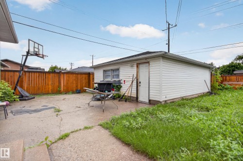 Detached garage with white siding and a wood door, complemented by a concrete patio and perimeter wood fencing - 9315 132A Avenue, Edmonton, AB 