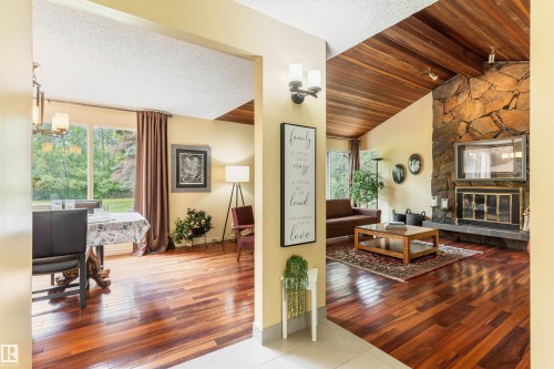 Spacious living area featuring rich wood-finish flooring, a vaulted wood plank ceiling, and a prominent stone fireplace with a black metal insert - 20515 5 Avenue Sw, Edmonton, AB 