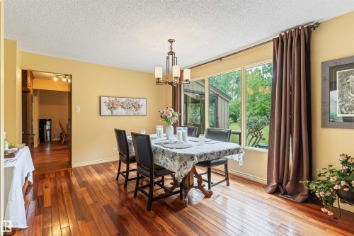 Dining area featuring wood-finish flooring, a contemporary chandelier, and a large window overlooking exterior greenery - 20515 5 Avenue Sw, Edmonton, AB 