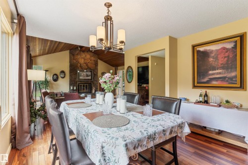 Dining area featuring wood-finish flooring, a contemporary chandelier, and a stone-clad fireplace - 20515 5 Avenue Sw, Edmonton, AB 