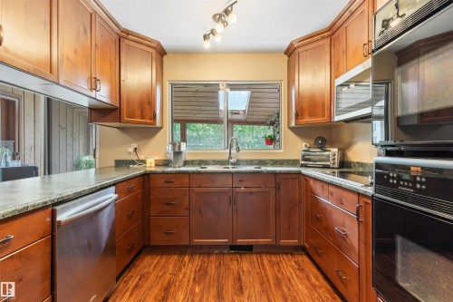 U-shaped kitchen featuring wood-finish cabinetry, stone-finish countertops, and wood-finish flooring - 20515 5 Avenue Sw, Edmonton, AB 