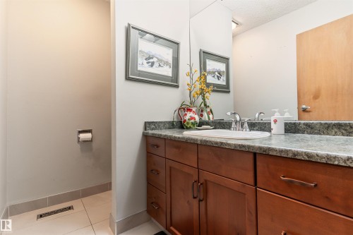 Bathroom vanity featuring a stone-finish countertop, undermount sink, and wood-finish cabinetry with multiple drawers and doors - 20515 5 Avenue Sw, Edmonton, AB 