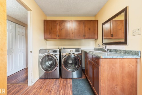 Dedicated laundry area featuring a utility sink, wood-finish cabinetry, and wood-finish flooring - 20515 5 Avenue Sw, Edmonton, AB 