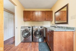 Dedicated laundry area featuring a utility sink, wood-finish cabinetry, and wood-finish flooring - 