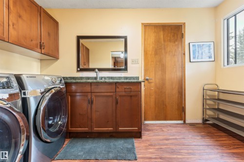 Laundry area featuring wood-finish flooring, a vanity with a sink and storage cabinetry, upper cabinetry, a window, and a wood-paneled door - 20515 5 Avenue Sw, Edmonton, AB 