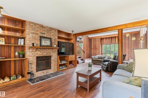 Living area featuring a brick fireplace with a black stone hearth, built-in wood shelving, wood-finish flooring, and exposed wood beams - 20515 5 Avenue Sw, Edmonton, AB 