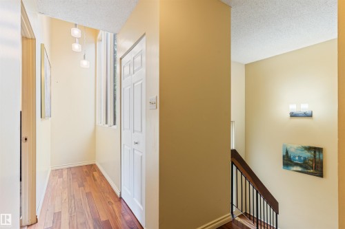 Hallway featuring wood-finish flooring, a bi-fold closet door, and a three-light pendant fixture - 20515 5 Avenue Sw, Edmonton, AB 