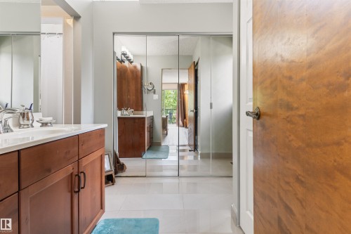 Bathroom featuring a wood-finish double vanity with white countertop, chrome fixtures, mirrored closet doors, and light tile flooring - 20515 5 Avenue Sw, Edmonton, AB 