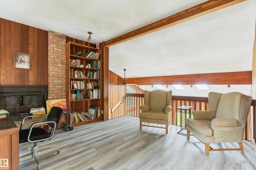 Lounge area featuring wood-finish flooring, a brick-surround fireplace with a dark mantel, and built-in wood shelving - 20515 5 Avenue Sw, Edmonton, AB 