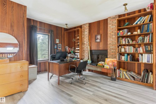 Room featuring wood-finish wall paneling, light wood-finish flooring, a brick fireplace surround, and built-in wood shelving units - 20515 5 Avenue Sw, Edmonton, AB 