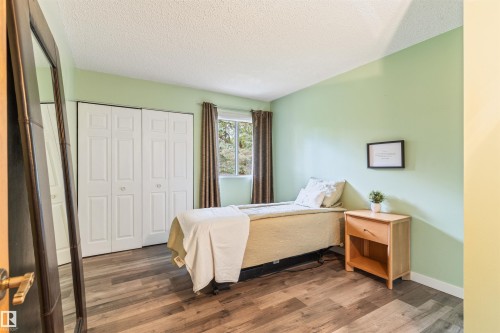 Bedroom featuring wood-finish flooring, a window with dark drapes, and bi-fold closet doors - 20515 5 Avenue Sw, Edmonton, AB 