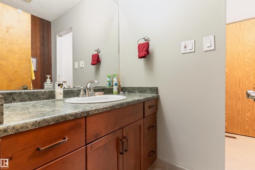 Vanity featuring a drop-in sink with a chrome faucet, a stone-finish countertop, and rich wood-tone cabinetry - 20515 5 Avenue Sw, Edmonton, AB 