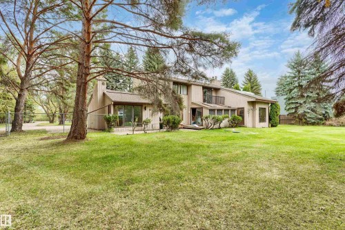 Expansive lawn with mature trees bordering a multi-level residence featuring a balcony, sliding glass doors, and a sunroom - 20515 5 Avenue Sw, Edmonton, AB 