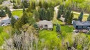 Expansive lot featuring a multi-story residence with a brown shingle roof, surrounded by mature evergreen and deciduous trees - 20515 5 Avenue Sw, Edmonton, AB 