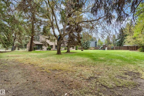 Expansive rear lawn framed by mature trees, featuring a light-toned exterior with multiple windows and a private patio - 20515 5 Avenue Sw, Edmonton, AB 