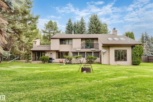Expansive rear exterior featuring a large lawn, mature trees, and a second-story balcony - 20515 5 Avenue Sw, Edmonton, AB 