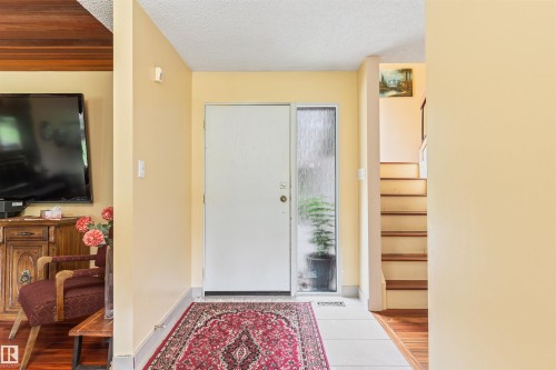Entryway featuring a white door with a frosted sidelight, white floor tiles, and a staircase with wood-finish treads - 20515 5 Avenue Sw, Edmonton, AB 