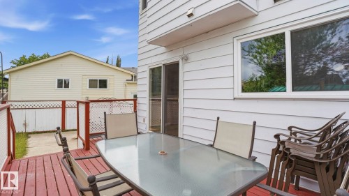 Outdoor deck featuring red-stained wood planking, white lattice railing accents, and a sliding glass door entry to the building - 1827 36 Street Nw, Edmonton, AB 