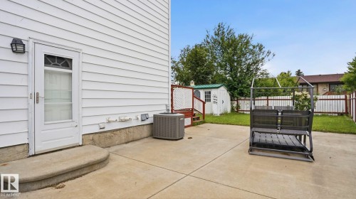 Rear concrete patio with a curved step entry, white siding, and an exterior light fixture - 1827 36 Street Nw, Edmonton, AB 