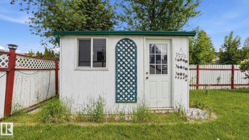 White storage shed with a green roof trim, featuring a single window and a paneled door with glass inserts - 1827 36 Street Nw, Edmonton, AB 