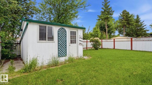 White outbuilding with a green-trimmed roof, featuring a window and an entry door with a decorative trellis - 1827 36 Street Nw, Edmonton, AB 