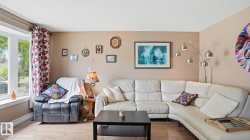 Spacious living area featuring light-toned walls, wood-finish flooring, and a large bay window - 1827 36 Street Nw, Edmonton, AB 
