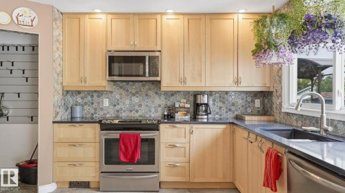 Kitchen featuring light wood cabinetry, stainless steel appliances, dark countertops, and a patterned tile backsplash - 1827 36 Street Nw, Edmonton, AB 