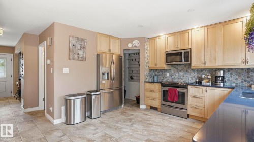 Kitchen featuring light wood cabinetry, stainless steel appliances, blue countertops, and a patterned tile backsplash - 1827 36 Street Nw, Edmonton, AB 