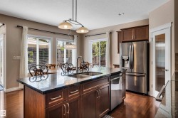 Kitchen featuring a central island with a dual-basin sink, dark stone-finish countertop, and wood-finish cabinetry - 
