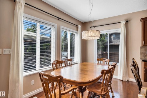 Dining area featuring wood-finish flooring, multiple windows with blinds, and a contemporary drum pendant light - 18 Voleta Crest, Spruce Grove, AB 