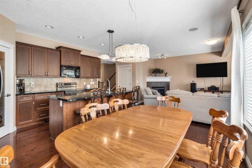 Open-concept living space featuring a dining area with a modern chandelier, a kitchen with dark cabinetry, granite-style countertops, and a tile backsplash, and a living room with a fireplace - 18 Voleta Crest, Spruce Grove, AB 