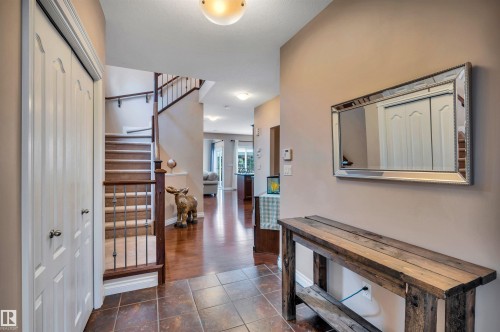 Inviting entryway with durable tile flooring and a contrasting wood-finish staircase featuring carpeted treads and wrought iron balusters - 18 Voleta Crest, Spruce Grove, AB 
