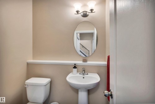 Powder room featuring a pedestal sink, oval mirror, and wall-mounted light fixture - 18 Voleta Crest, Spruce Grove, AB 