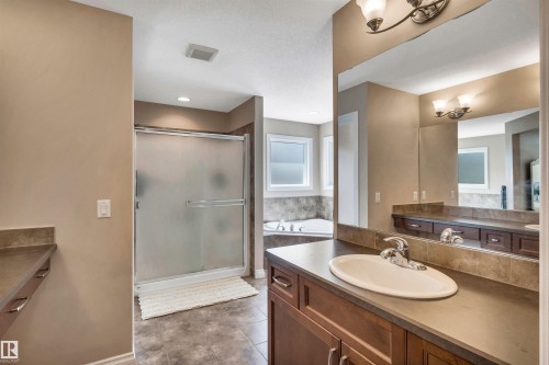 Bathroom featuring a single vanity with an oval basin, a large wall mirror, a separate shower with a frosted glass door, a corner soaking tub, and tile flooring - 18 Voleta Crest, Spruce Grove, AB 